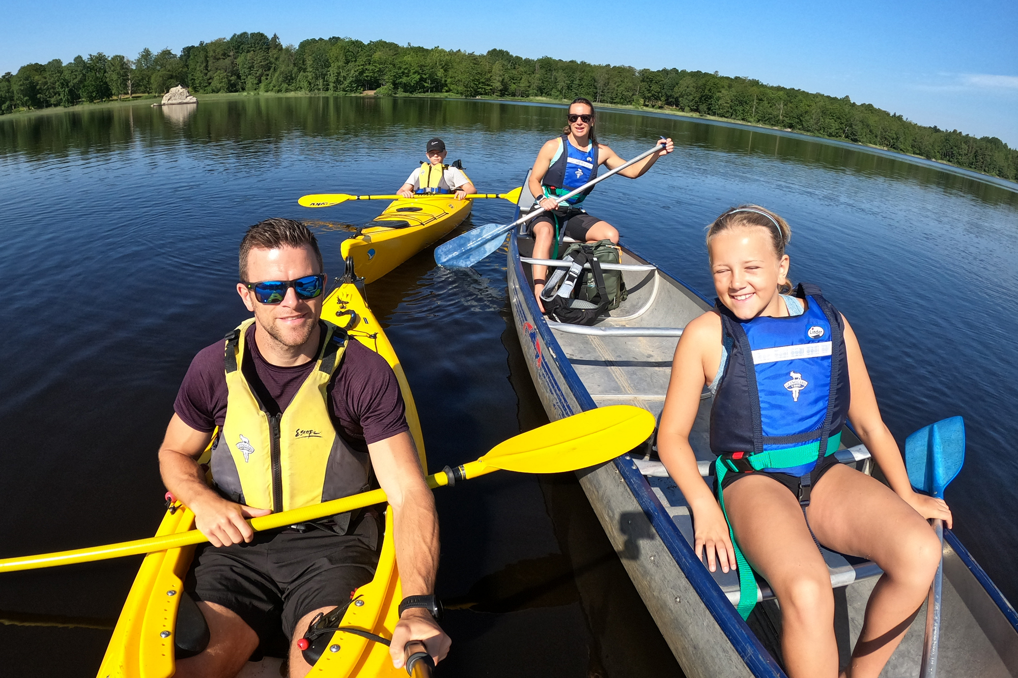 Team Lost med familj paddlar kajak på en småländsk sjö och tittar leende in i kameran med flytvästar på sig