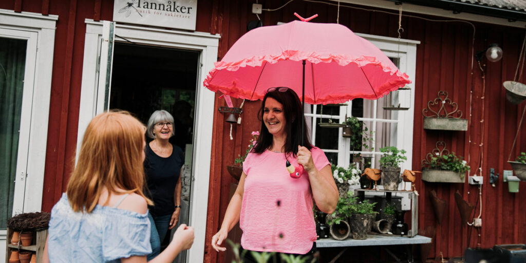 Tre kvinnor står utanför ett hus. En kvinna har ett paraply och ler.